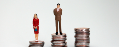 Figurine woman and man standing on different sized coin piles, with the man's pile higher